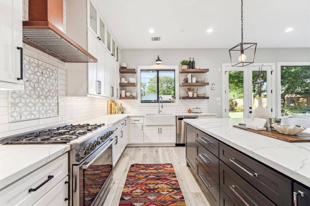 This spacious, modern living room features large windows and French doors that open to a backyard, offering plenty of natural light. The custom built-in shelving around a TV nook and stylish wood-look flooring create an inviting atmosphere for relaxation and entertainment.