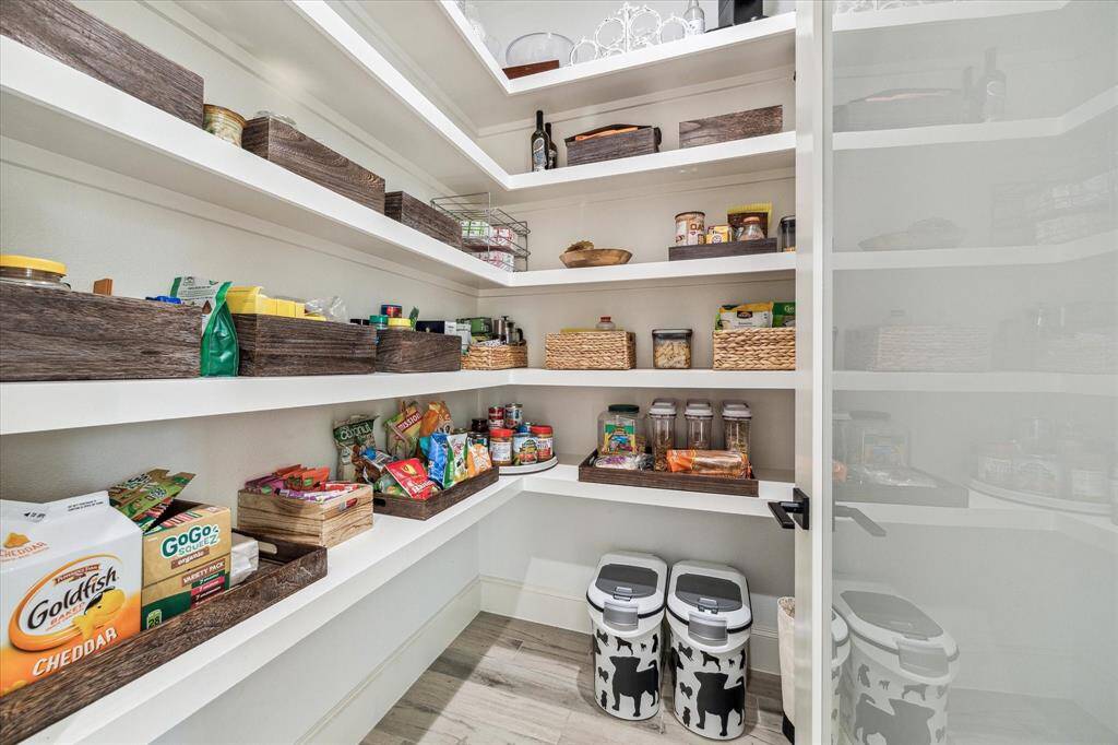 This kitchen features a modern design with a large island and room for four barstools. It includes white cabinetry with soft close drawers, stainless steel appliances, and open shelving, complemented by a sleek black and white color scheme. Pendant lights add a stylish touch, and a window provides natural light.