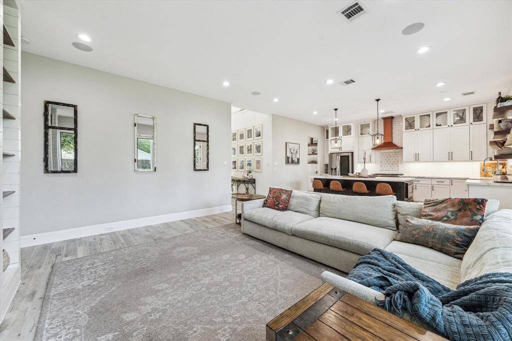 This modern kitchen boasts a stylish tile backsplash, high-end stainless steel appliances, open shelving, and ample natural light from the window and glass doors leading to the backyard. Perfect for cooking and entertaining.