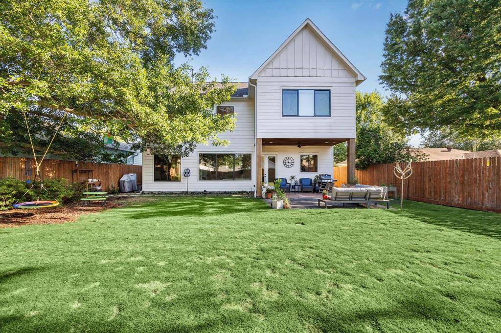 This photo showcases a spacious backyard featuring a covered patio with a wooden ceiling and fan. The area is beautifully landscaped with a mix of greenery, paving, and seating, creating a perfect outdoor retreat.