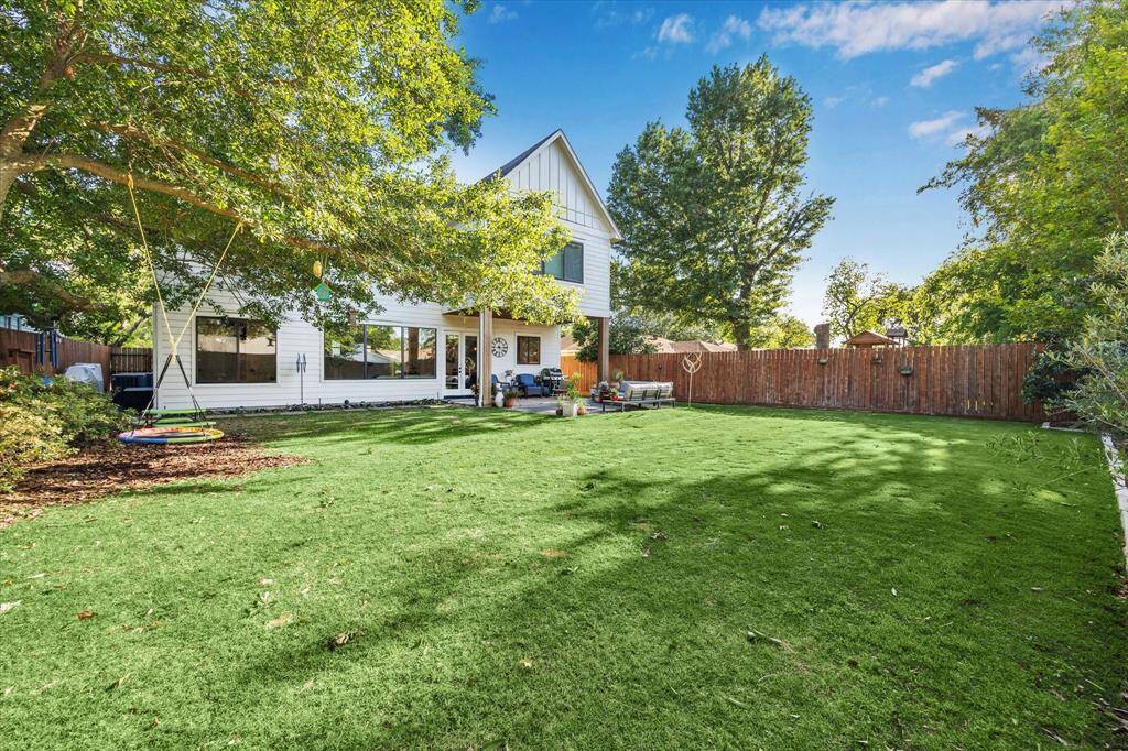 Enjoy this spacious backyard with lush green grass, mature trees, and a cozy patio area perfect for outdoor entertaining and a wooden fence for privacy.
