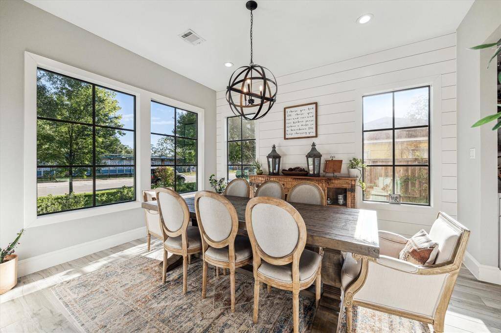 Charming and welcoming entryway featuring a wooden door, cozy seating area, and tasteful landscaping with potted plants and shrubs. The modern design includes large windows and a well-maintained path leading to the entrance.