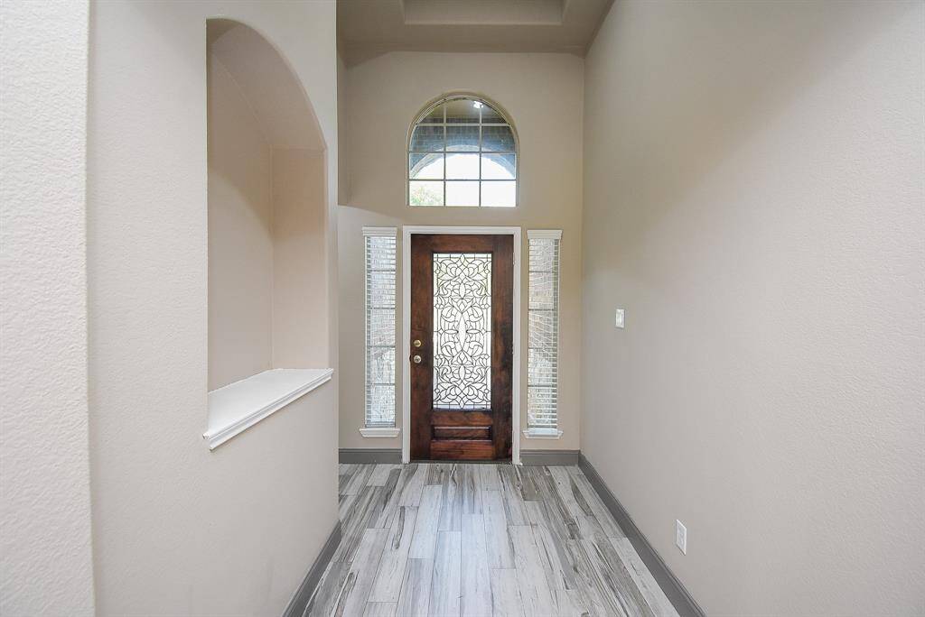 Welcoming entryway featuring elegant tile flooring, a stylish transom window, and a decorative glass front door, inviting natural light and warmth.