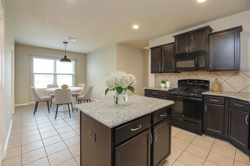 Spacious kitchen with elegant dark cabinetry, granite countertops, and a cozy dining area filled with natural light. Perfect for culinary enthusiasts and family gatherings. Virtual staging was used.