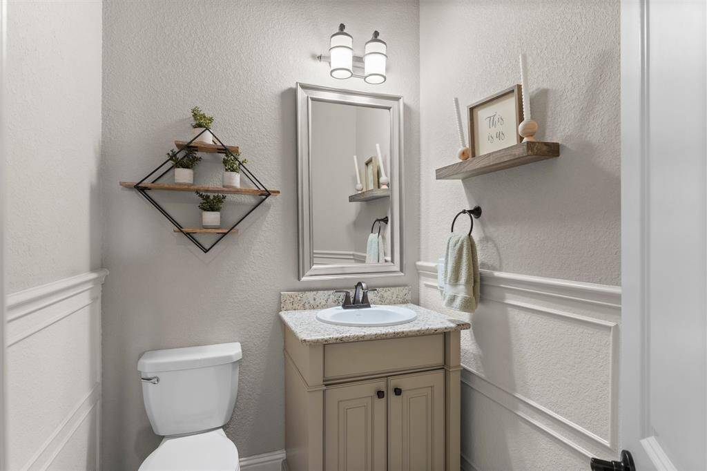 This photo showcases a cozy, well-lit half bathroom with elegant wainscoting, a granite countertop, and modern fixtures.