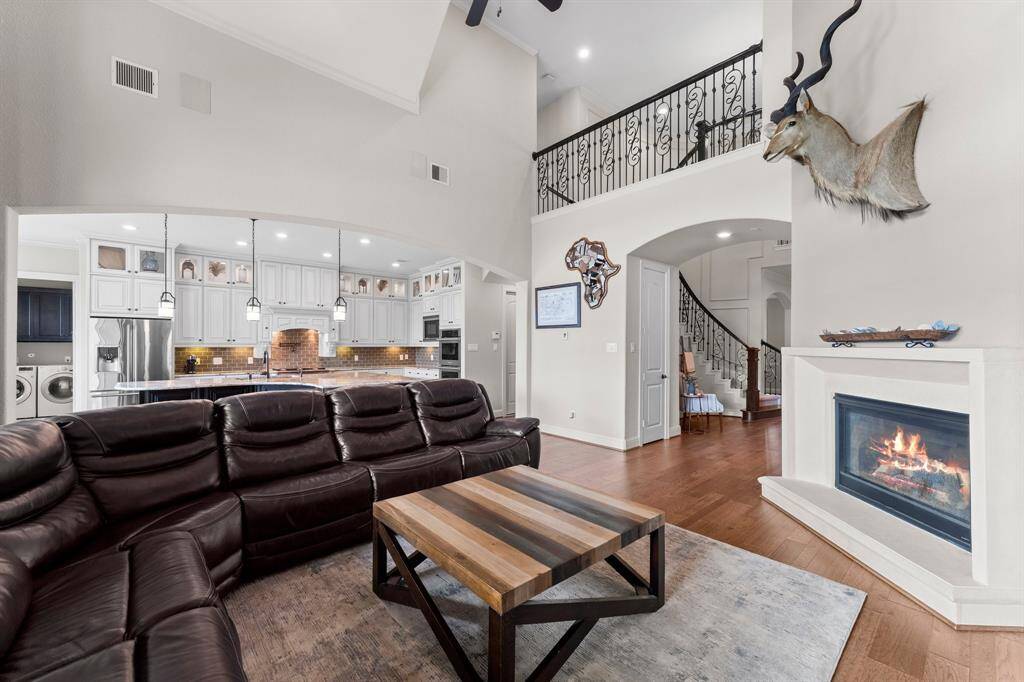This inviting living space features a cozy fireplace and hardwood floors. The open-concept design flows seamlessly into a modern kitchen with stainless steel appliances and elegant pendant lighting. A staircase with wrought iron railings leads to an upper level, creating a spacious and airy atmosphere.