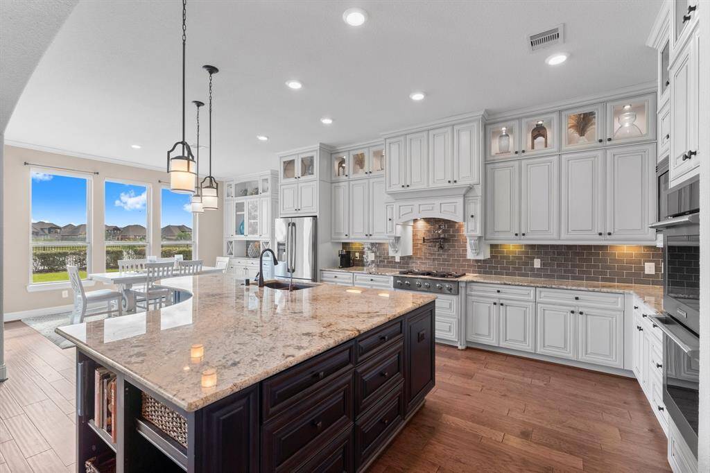 This elegant kitchen features a spacious island with granite countertops, pendant lighting, and ample cabinetry. It opens to a dining area with large windows offering scenic views, blending style with functionality.