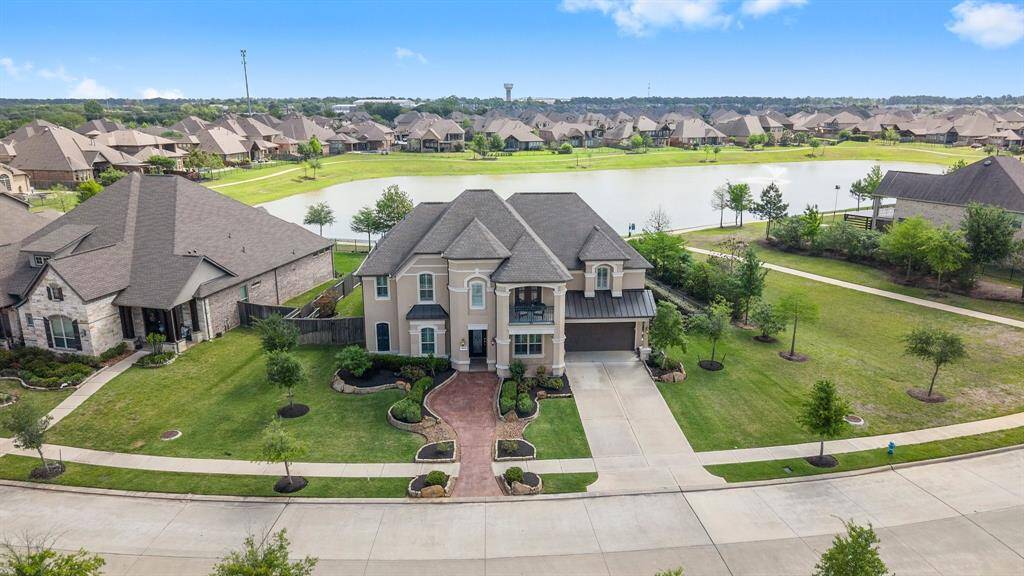 This photo showcases a spacious, elegant two-story home with a landscaped front yard and a driveway. It's located in a suburban neighborhood, offering scenic views of a nearby lake and walking paths.