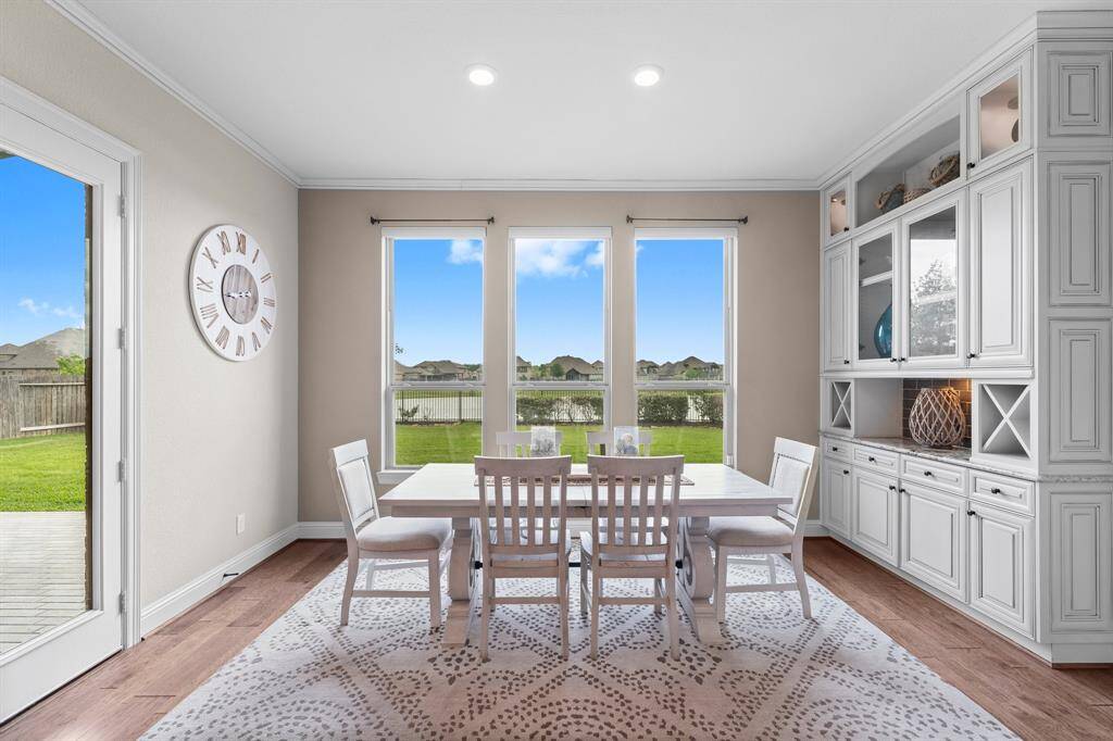 Bright dining area with large windows offering a scenic view, white cabinetry for storage, and a cozy wooden table set, perfect for family meals. The room opens to a lush backyard through a glass door.