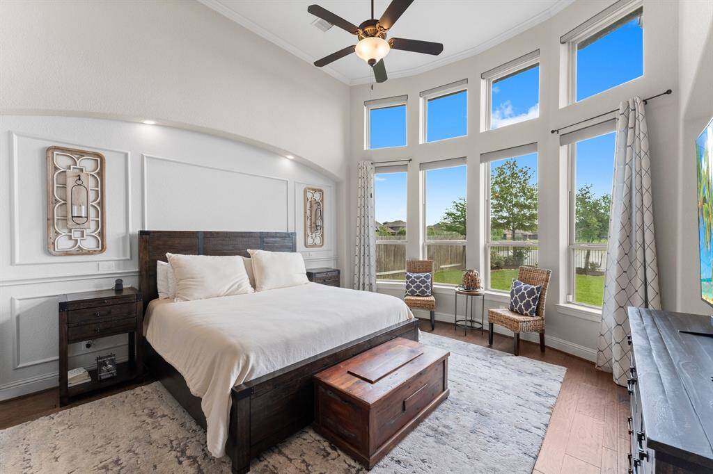 This spacious bedroom features large windows that provide abundant natural light and a scenic view of the backyard. It includes a stylish ceiling fan, and a cozy seating area.