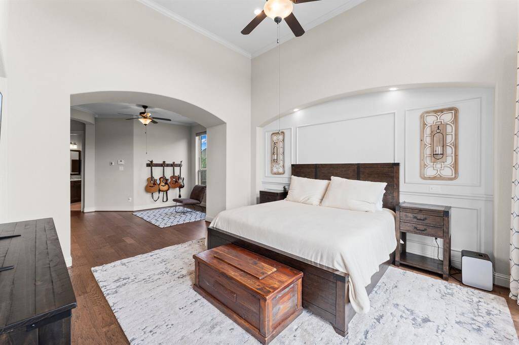 This spacious bedroom features a high ceiling with a fan, elegant archways, and hardwood floors. It includes a cozy seating area.