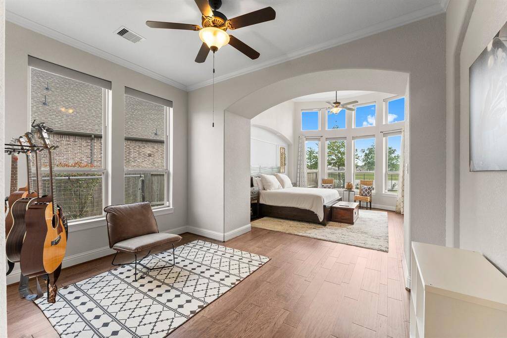 This bright and airy master bedroom features large windows with beautiful views, a cozy seating area, and a stylish archway leading to a spacious sitting nook.
