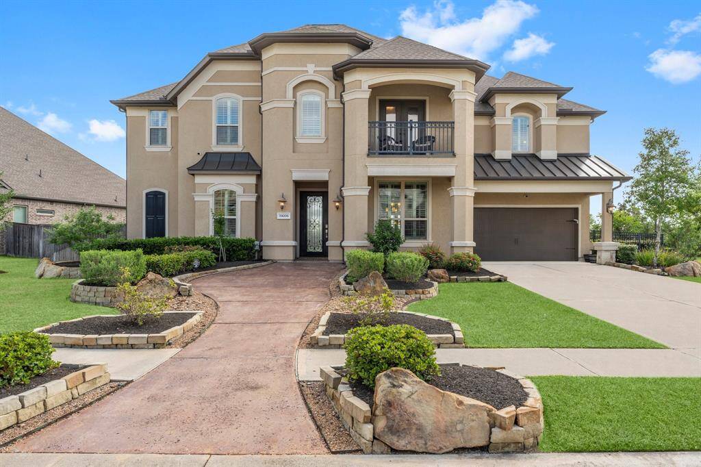This elegant two-story home features a grand facade with a welcoming front path, manicured landscaping, and a two-car garage. The stucco exterior, decorative pillars, and balcony add to its charm.
