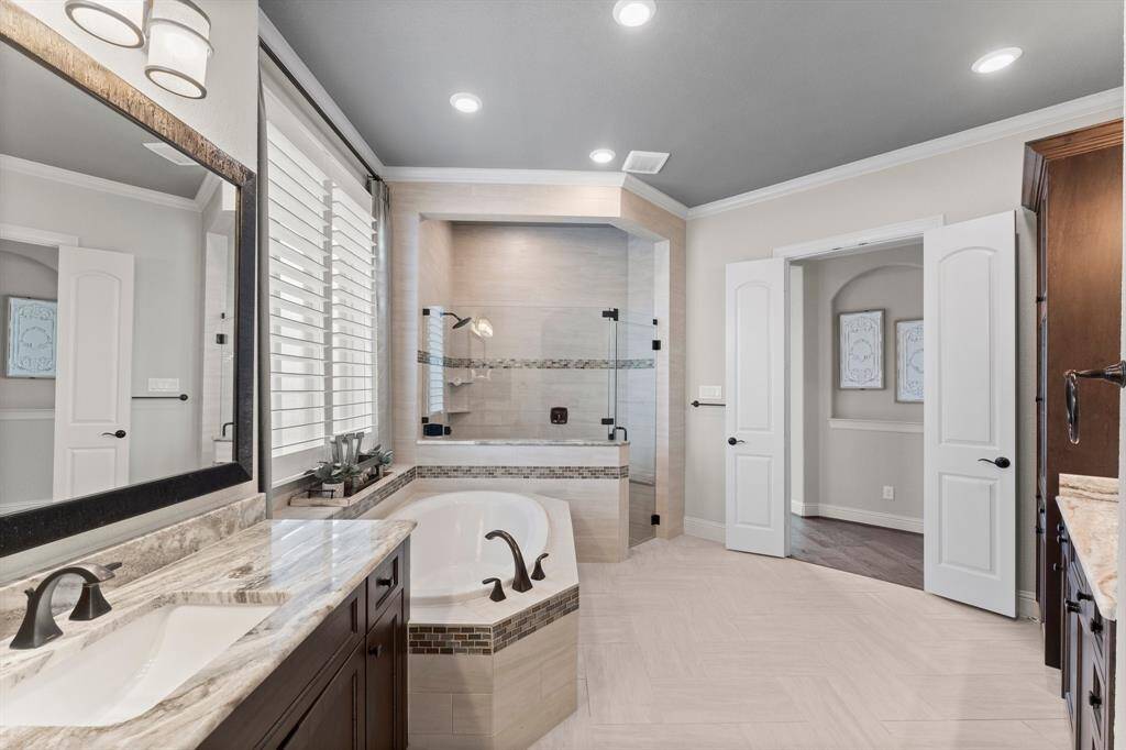This spacious bathroom features a sleek design with a large glass-enclosed shower, a luxurious soaking tub, and dual sinks with elegant fixtures. The room is bright with ample natural light, complemented by modern lighting and stylish tile work.
