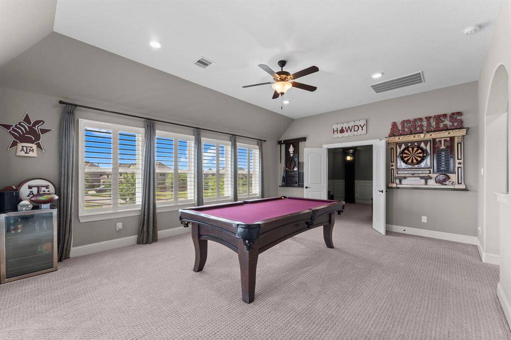 This spacious game room features a pool table, dartboard, and abundant natural light from large windows. It's perfect for entertaining, with a ceiling fan for comfort.