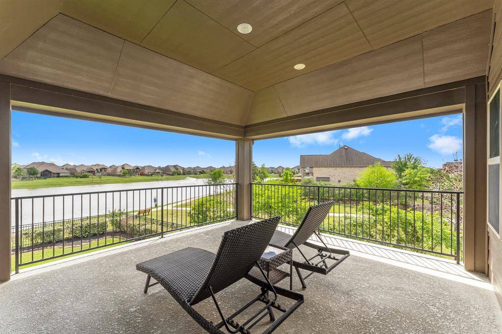 Spacious covered patio with relaxing lounge chairs, offering a scenic view of a serene lake and lush greenery, perfect for outdoor enjoyment.
