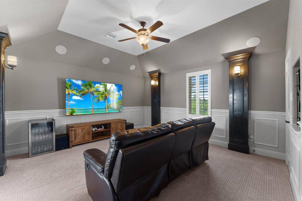 This home theater features a cozy setup with a large wall-mounted TV, comfortable leather seating, and built-in speakers. It includes a mini-fridge and is decorated with elegant wall sconces and wainscoting, creating a perfect entertainment space.