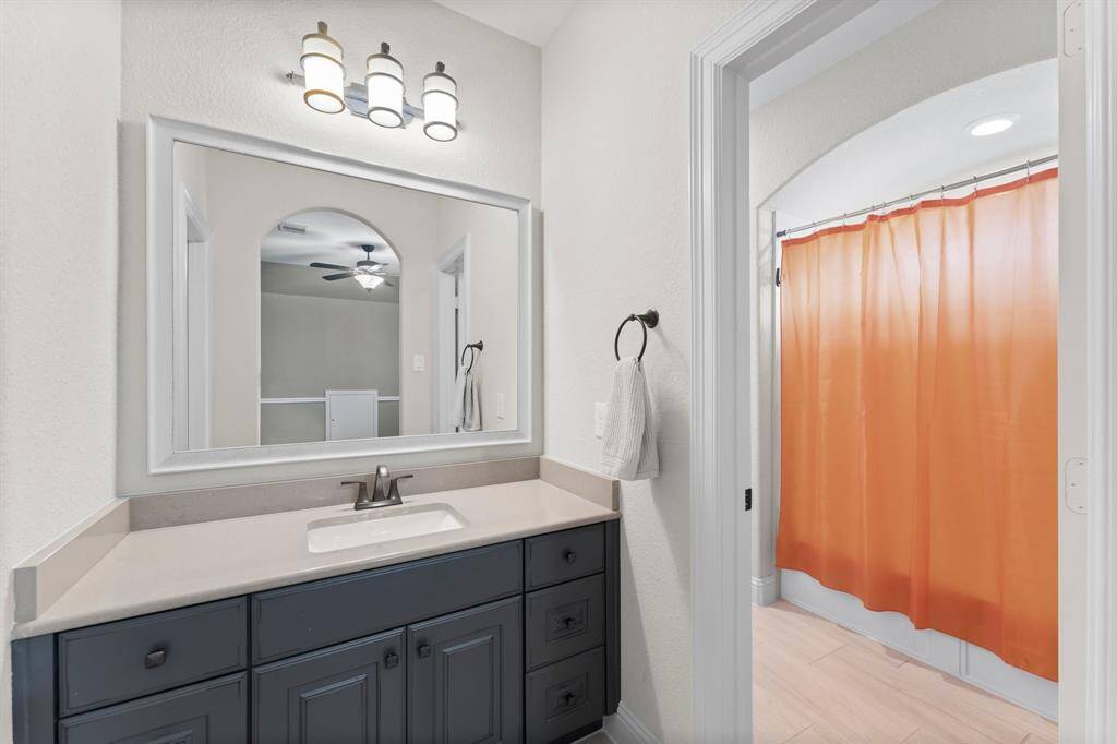This bathroom features a modern vanity with a large mirror, stylish lighting. It includes a separate shower area, offering a functional space.