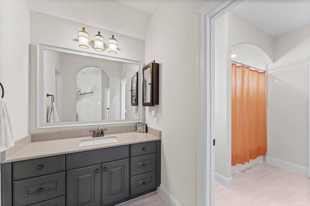 This bathroom features a modern vanity with a large mirror and dark cabinetry, complemented by stylish lighting. The adjacent area includes a shower.