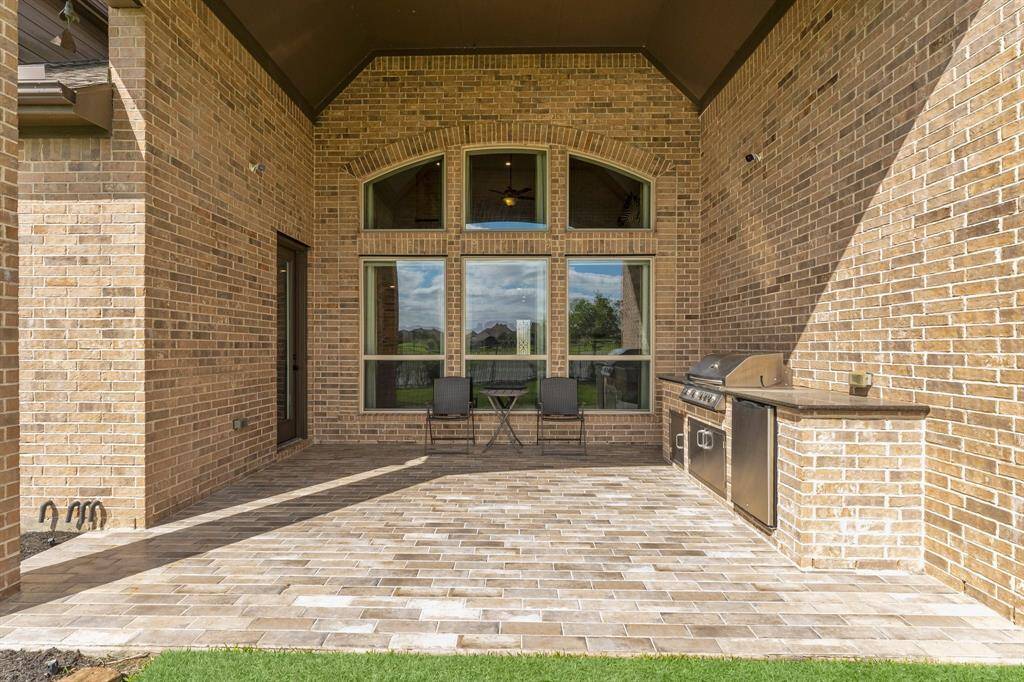 This photo showcases a spacious outdoor patio with brick walls and flooring, featuring a built-in stainless steel grill. Large arched windows enhance the space with natural light, making it perfect for entertaining or relaxing outdoors.