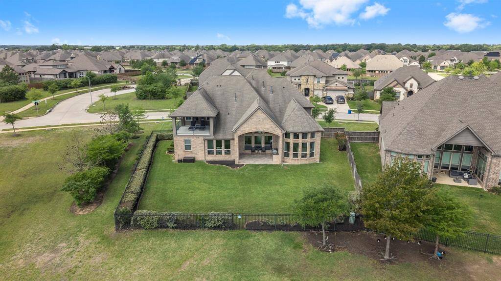 This aerial photo showcases a spacious, well-maintained brick home with a large fenced backyard. The property offers a generous lawn and a covered patio, ideal for outdoor enjoyment.