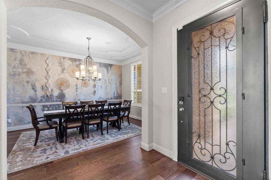 Elegant dining area with an artistic accent wall and chandelier, visible through an arched entryway.