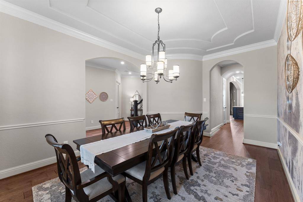 This elegant dining room features a stylish chandelier, and tasteful decor. The room boasts hardwood floors, soft neutral walls, and decorative molding, creating a warm and inviting atmosphere.