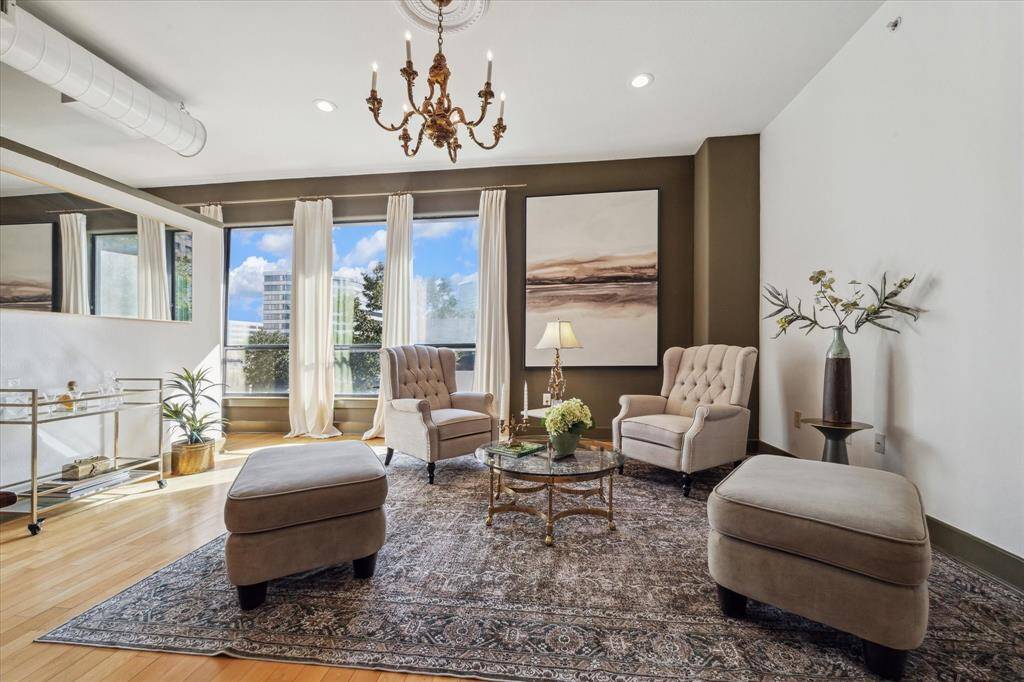 This is a bright and elegant living space featuring large windows with outside views, high ceilings with a classic chandelier, and a warm, neutral color palette.
