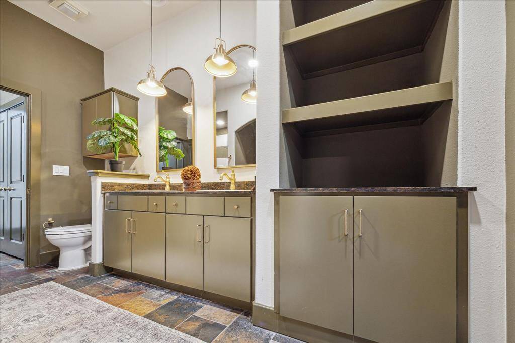 The bathroom features olive-green cabinetry with sleek hardware, granite countertops, dual arch-shaped mirrors above the vanity with stylish pendant lights, a mix of contemporary design and functionality.