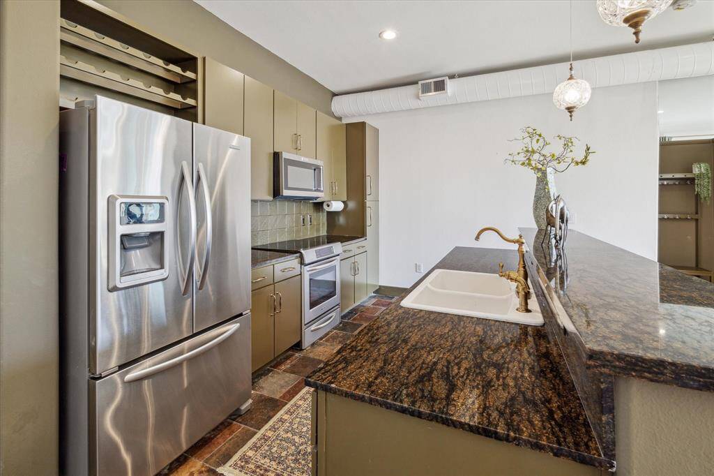 Imagine yourself in this modern kitchen featuring stainless steel appliances, including a refrigerator with water and ice dispenser and a microwave oven. There's a double sink with a unique faucet, ample cabinet storage, and granite countertops.