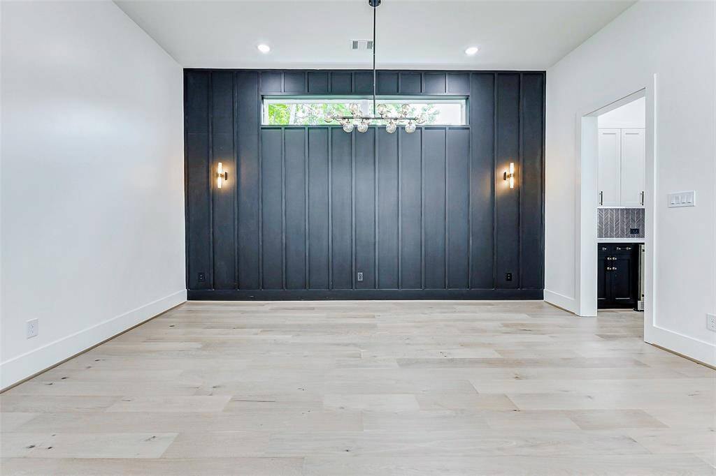 The dining area is a statement of modern elegance, featuring a striking black accent wall that adds depth and drama to the space. Suspended above, sleek, modern light fixtures create a warm, inviting ambiance, perfect for both intimate dinners and entertaining guests.
