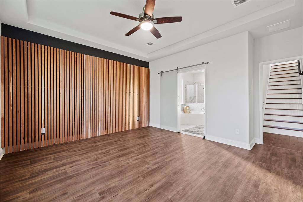 Downstairs primary bedroom with wood-look tile flooring, tray ceiling and an en-suite bathroom.