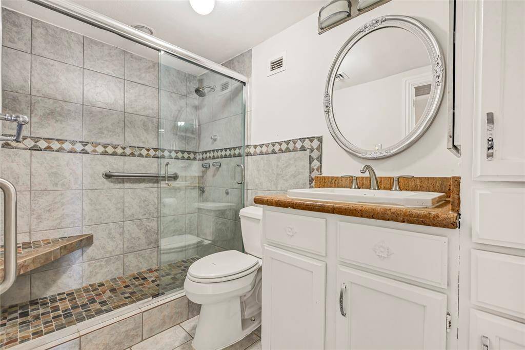 The primary bathroom offers a sleek glass-enclosed shower and a convenient single sink, creating a clean and functional space.