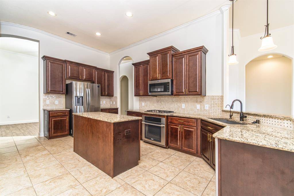 Kitchen with 42” cabinets, under-cabinet lighting, gas stove, granite countertops, refrigerator, and stainless steel appliances