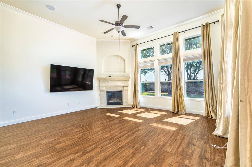 Bright and inviting living room with wood floors, fireplace, TV, and integrated ceiling speakers. Tall windows with blinds and drapes invite the sunshine indoors.
