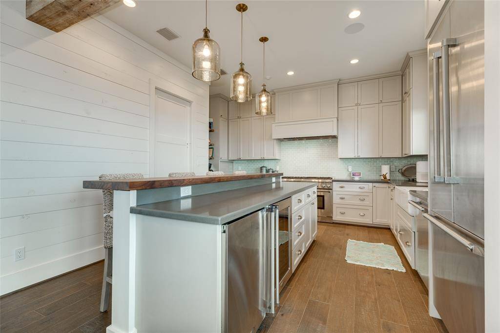 Large 2-tiered island has a secondary small refrigerator + wine cooler. Elevated breakfast bar is topped in butcher block