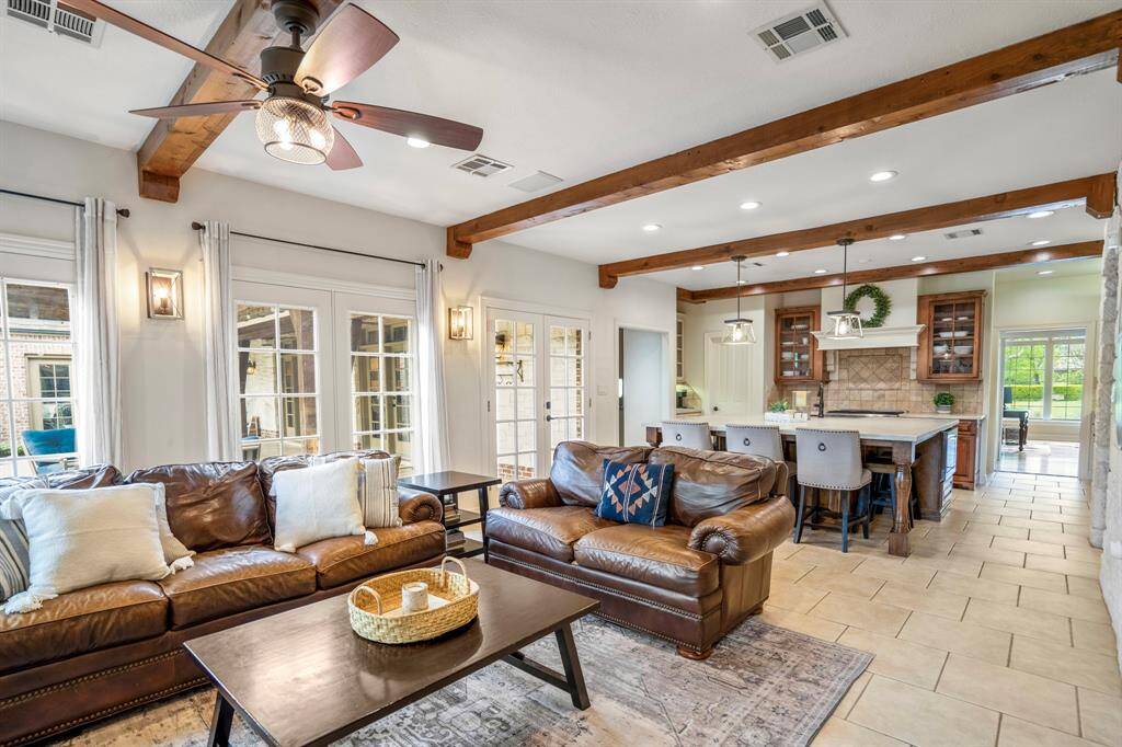 Experience open-concept elegance in this inviting living space, featuring rustic wood beams, cozy leather seating, and a seamless flow into a modern kitchen. Perfect for entertaining and relaxation.