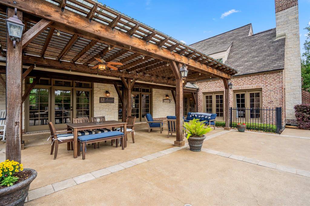 This inviting outdoor space features a spacious patio with a wooden pergola, perfect for entertaining. It includes comfortable seating, a dining area, and charming details like potted plants. The brick and stone exterior of the home adds a touch of elegance and warmth.