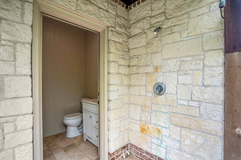 This photo features an outdoor stone shower with a nearby access to a small indoor bathroom. The bathroom makes hosting pool parties a breeze!