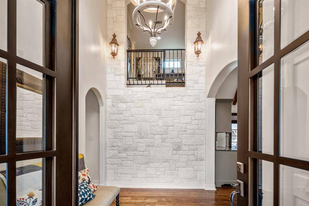 Welcome to an inviting foyer featuring elegant wood floors, a striking stone wall, a charming balcony, and ambient lanterns.
