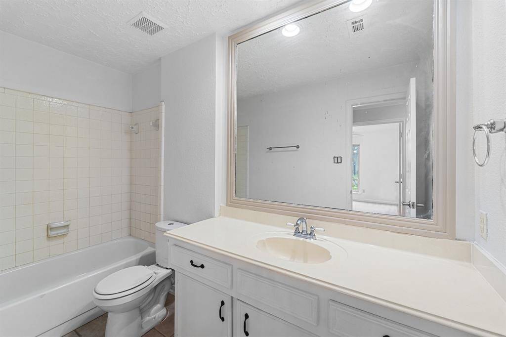 Secondary bathroom, featuring tile floors, a tub/shower combo with a gorgeous tile shower wall, white cabinets, and a large framed mirror.