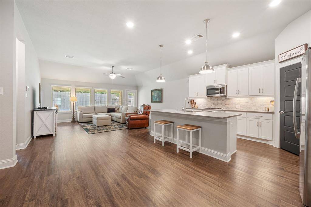 The open-concept design seamlessly integrates the kitchen and living areas, creating a spacious and inviting atmosphere typical of a ranch-style home. Large windows flood the space with natural light, enhancing the sense of openness diluting the lines between indoor and outdoor living.