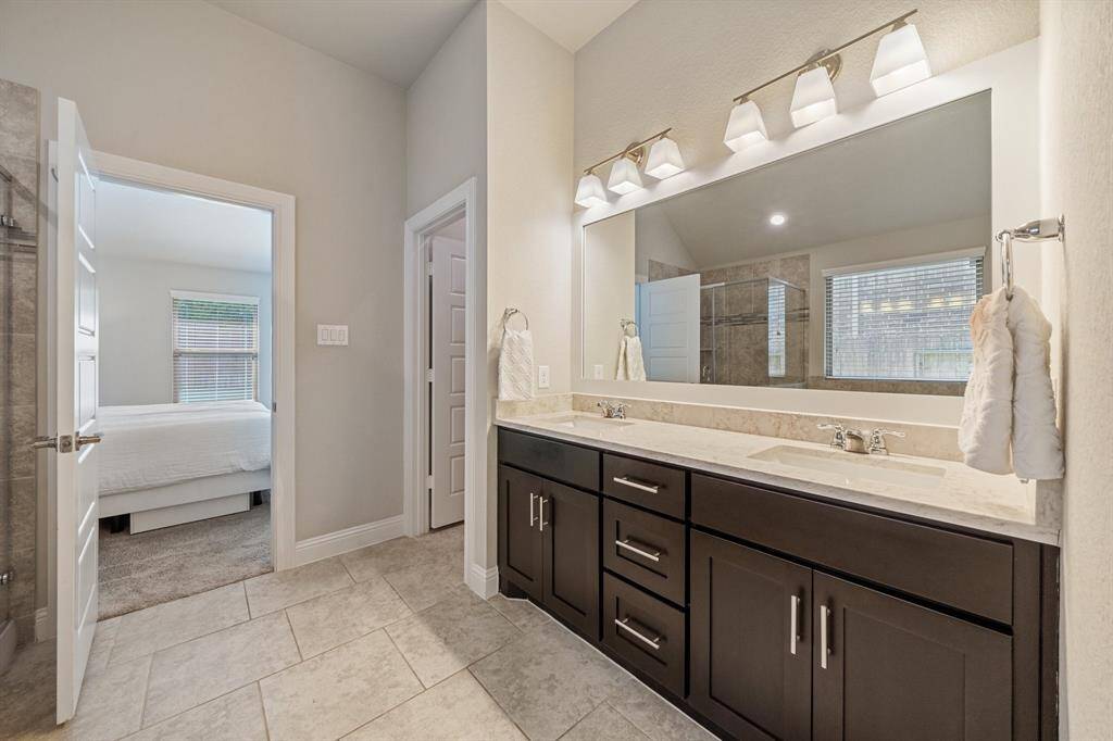 The master bathroom features a double sink vanity with dark wood cabinets and upgraded quartz countertops, creating a sleek and elegant look. The large framed mirror adds sophistication above the sinks and enough space for relaxation.
