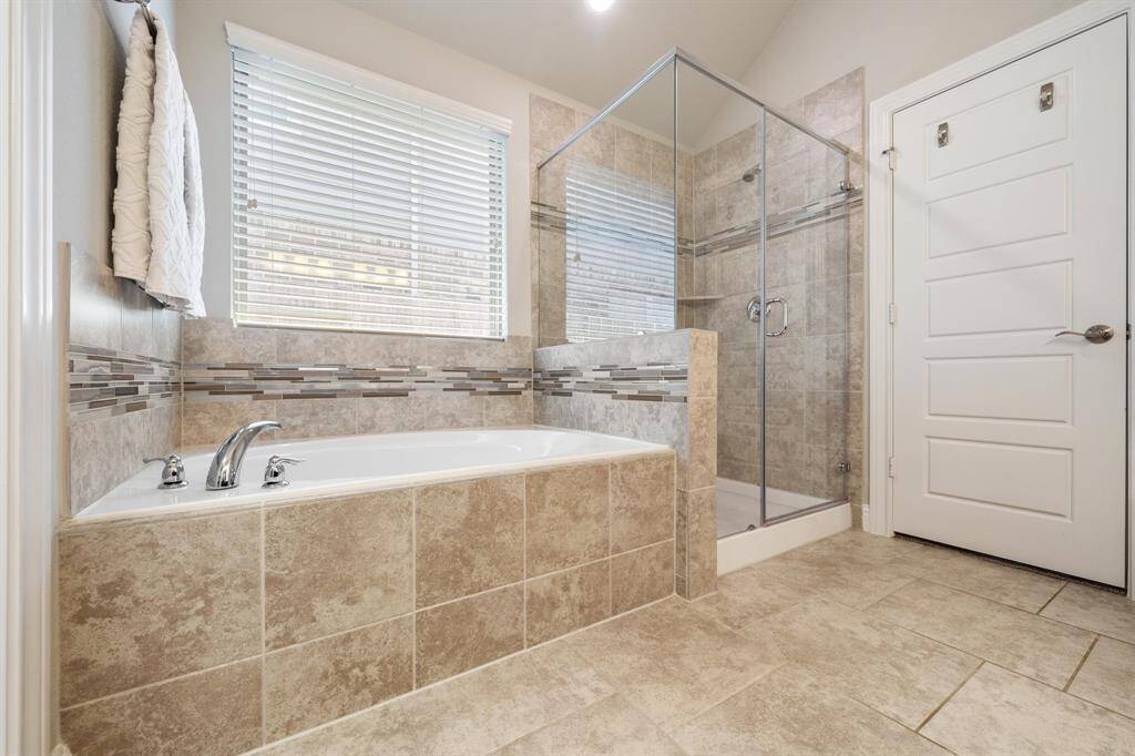 The bathroom features a spacious seamless glass shower situated next to a bathtub adorned with maple light brown tiles. The combination of modern glass accents and earthy tile tones enhances the overall elegance and comfort of the space.