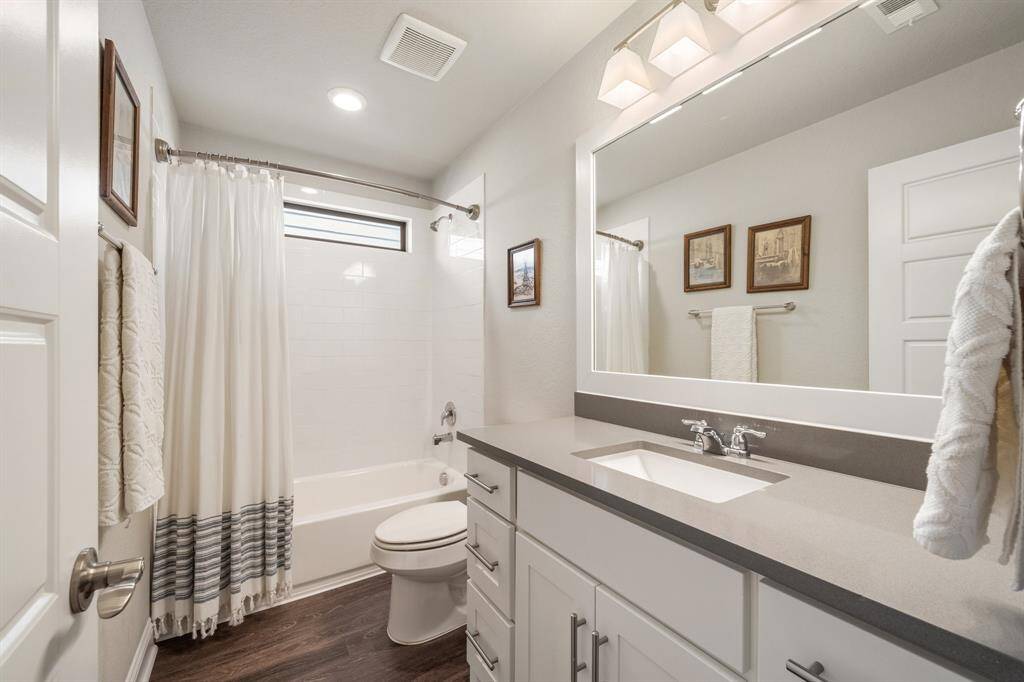 The secondary bathroom features a sleek vanity, also with quartz countertops, ample cabinet space, and a large framed mirror.