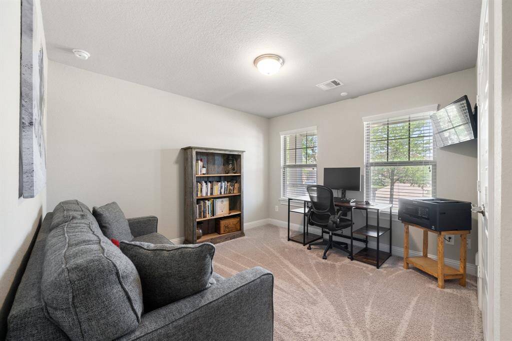 This versatile game room features plush carpeted flooring, a cozy gray sofa, and two mid-sized windows that bring in abundant natural light. Elegant white baseboards add a refined touch to the clean and inviting space.