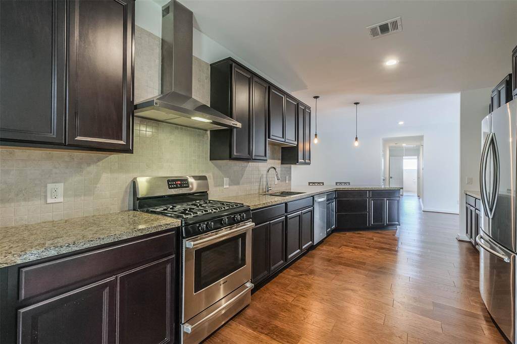 Gas range and large overhead exhaust with the neutral colored travertine backsplash behind it.