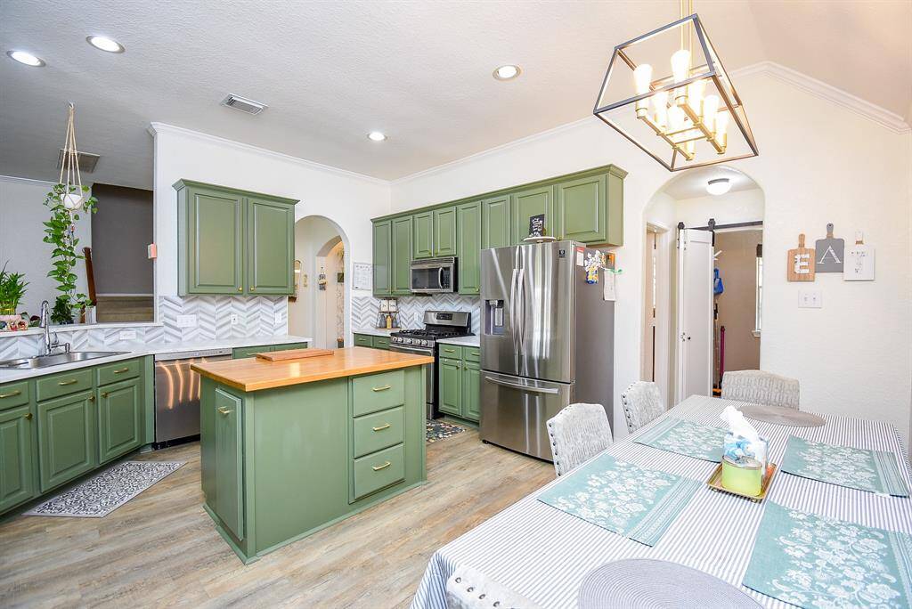 This kitchen features olive green cabinetry, a stainless steel fridge, and a central island with wooden countertop. It includes a modern breakfast area with stylish lighting, creating a cozy and functional space for cooking and dining.