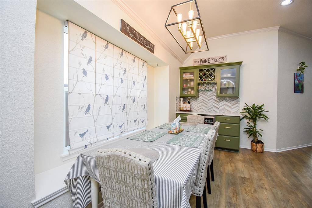 This breakfast area features a cozy setup, a modern light fixture and a stylish green cabinet with a wine rack.