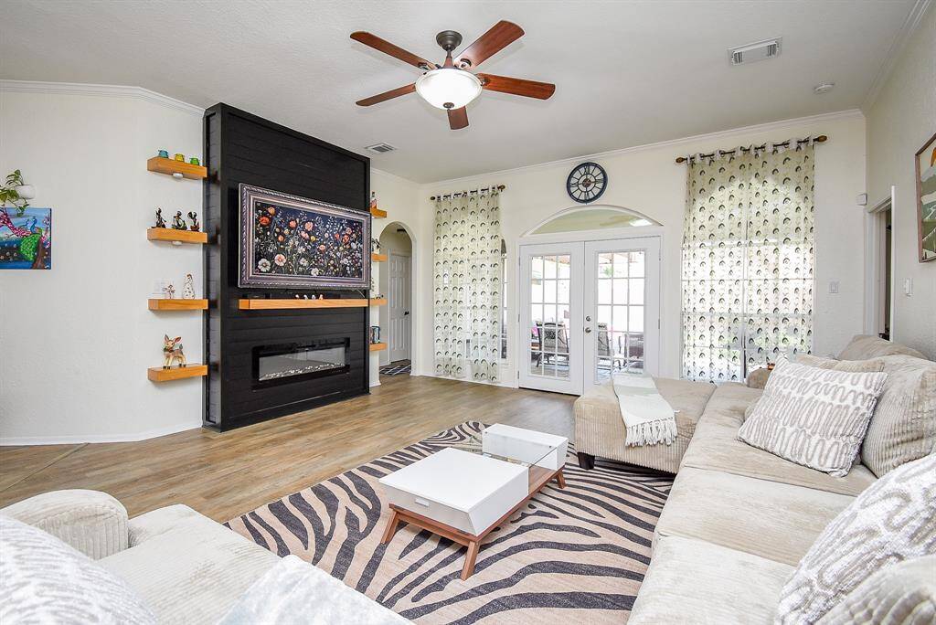 This spacious living room features a modern fireplace, elegant shelving, and large windows. It has a bright, welcoming atmosphere with easy access to a patio through French doors.
